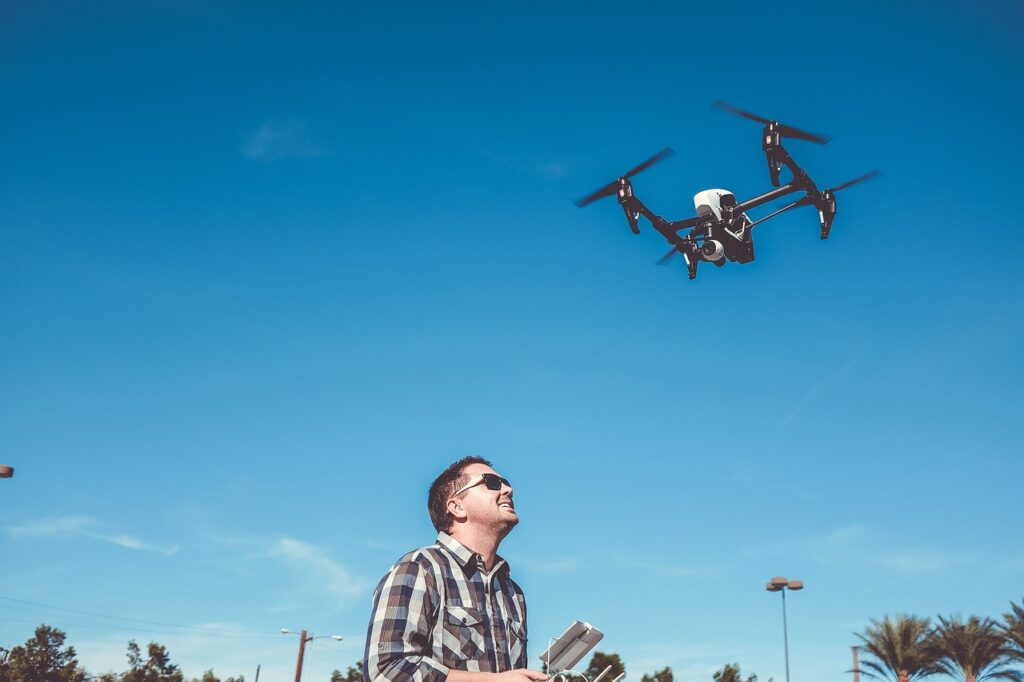 A man in a checkered long-sleeves controlling a black drone in the neighborhood