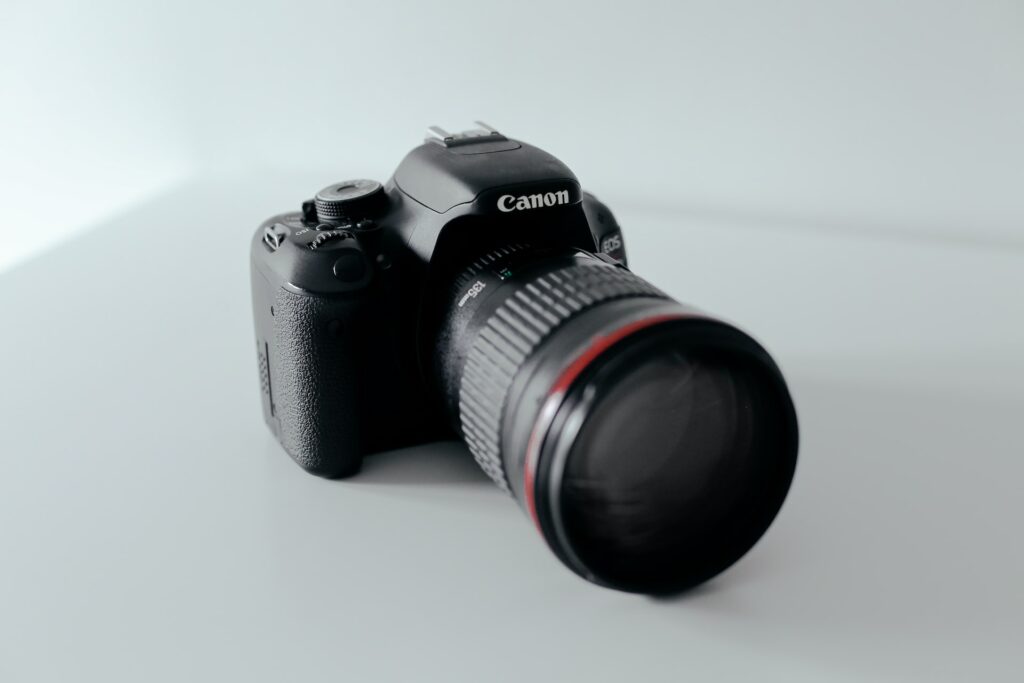 A black Canon SLR camera on top of a white surface and near a white background