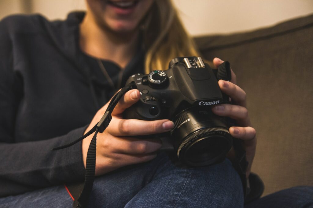 A woman with blonde hair and wearing a black hoodie is holding a black Canon SLR camera