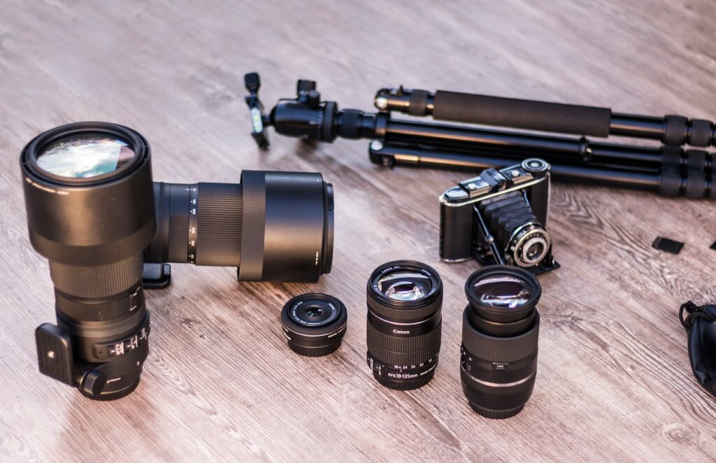 Black analog camera and different camera lenses and a black tripod placed on a wooden surface