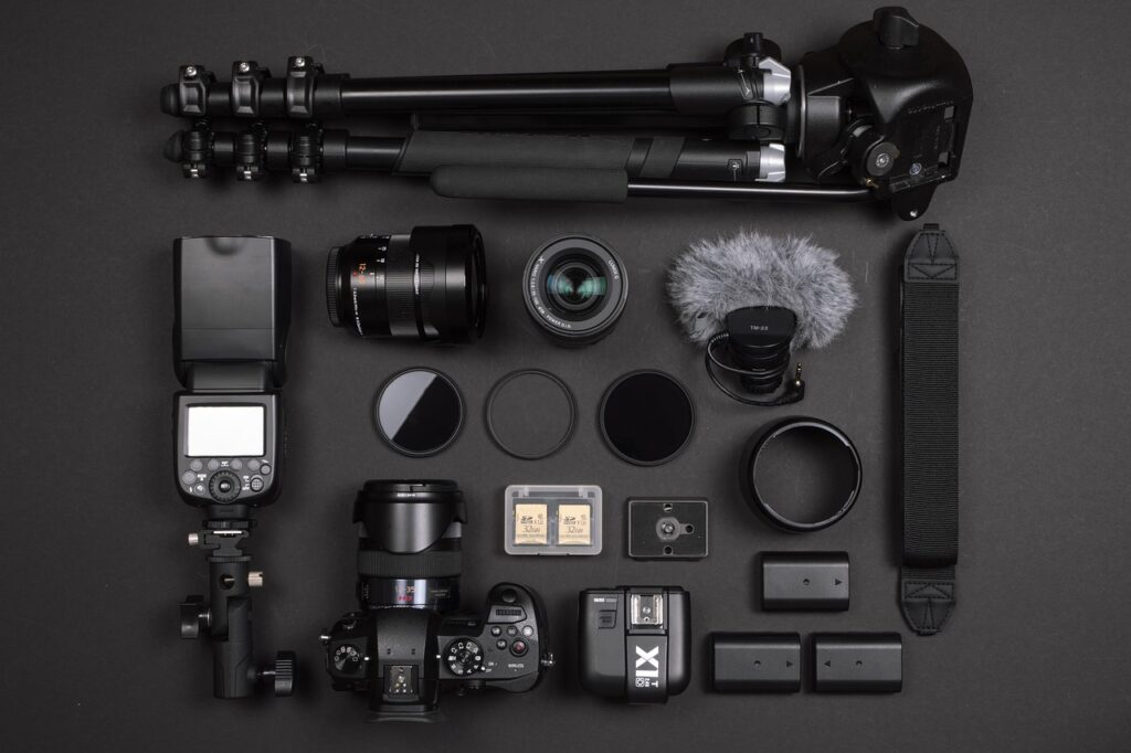 Camera equipment like a black DSLR camera, lenses, external flash, and tripod placed on a black surface