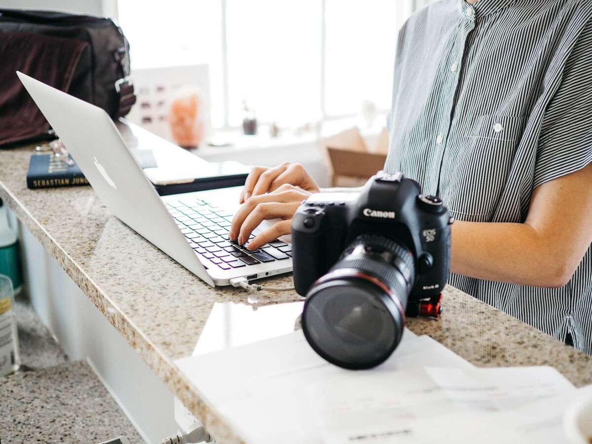 A person wearing a black and white striped blouse while using a silver laptop near a black Canon camera on top of a marbled table