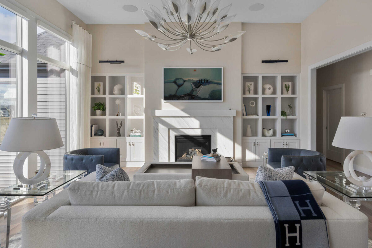 A modern living room with a neutral color palette, featuring a fireplace, built-in shelves, elegant furniture, and a statement chandelier.