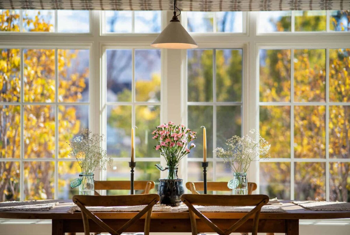 Three different flowers in vases on a classic wooden table with the perfect background of the fall leaves as seen on the wide glass windows
