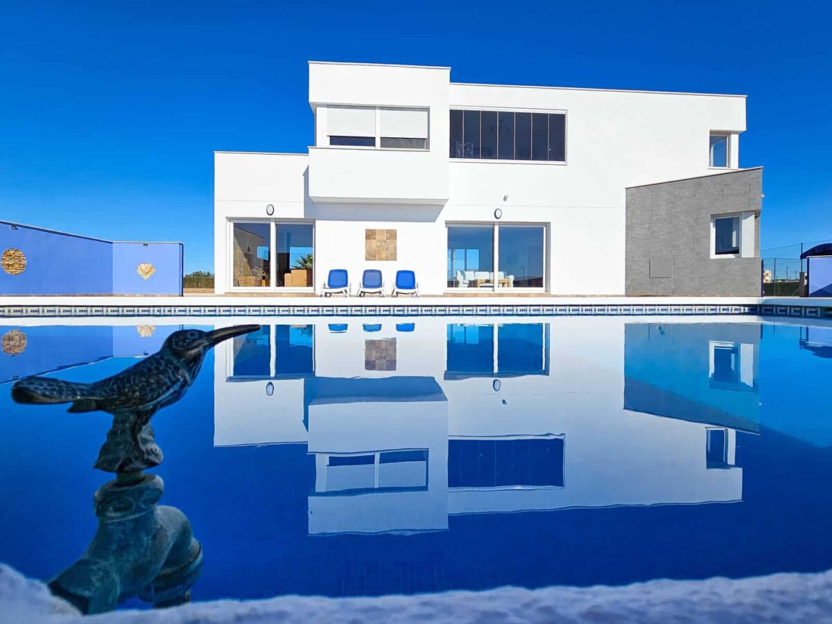 Two story house with a wide pool reflecting the exterior of the house