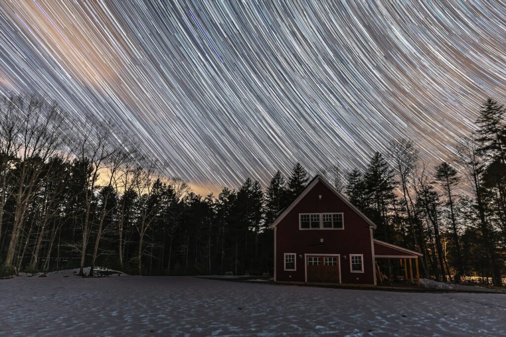 A big brown house with an expansive front yard near tall tress under the starry sky