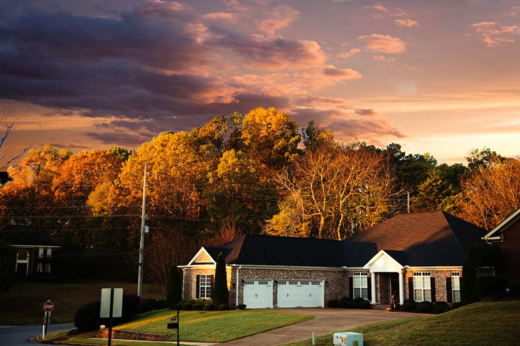 A house with a brown roof and white garage doors with a scenic view of tall trees near an empty street