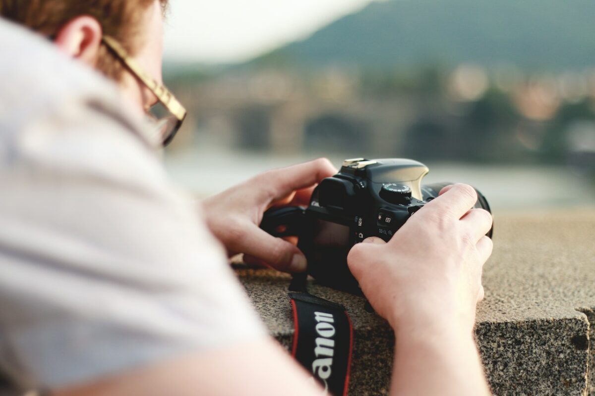 A man in a white top setting up a black Canon DSLR camera on a gray concrete ledge