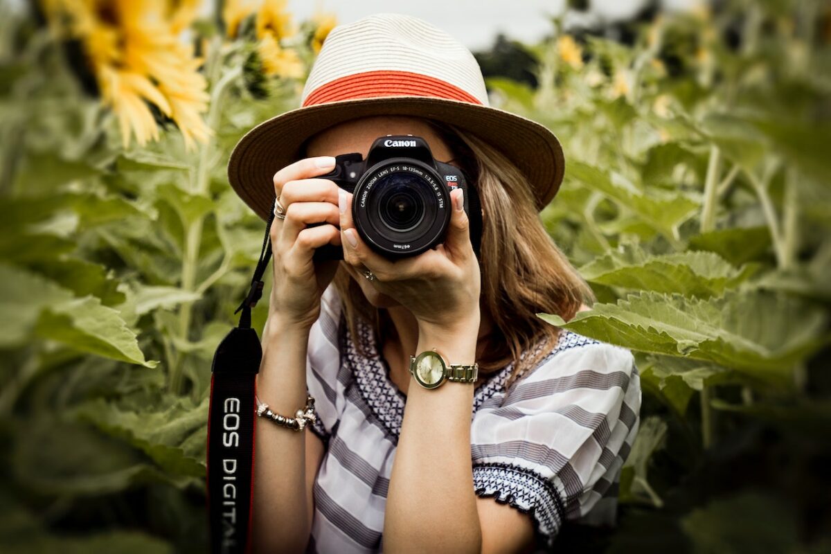 A woman wearing a blouse uses a black Canon DSLR camera