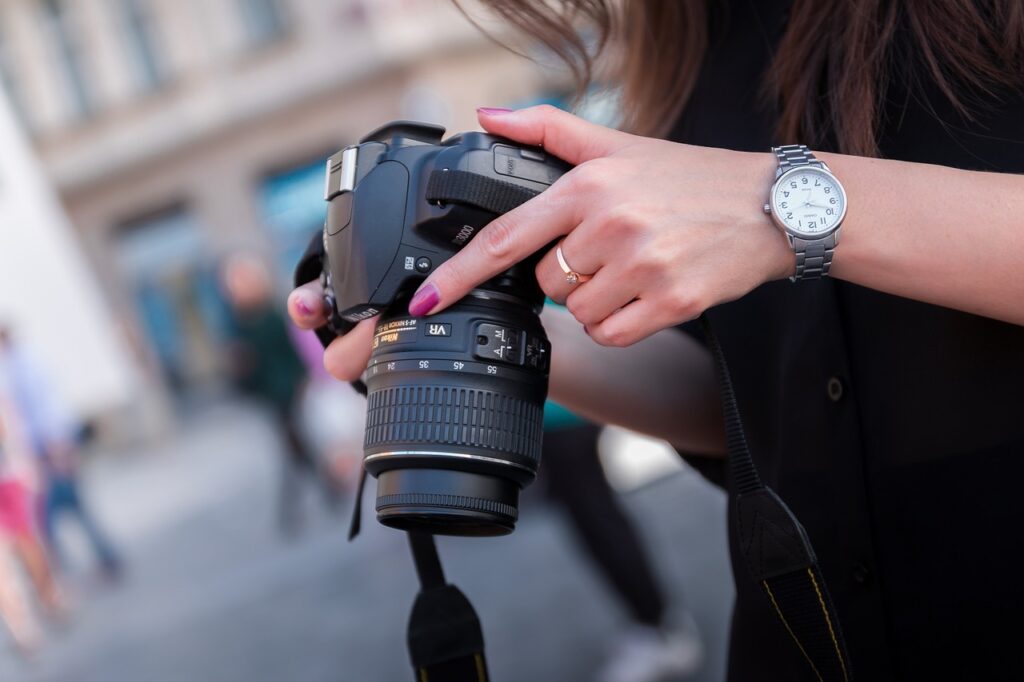 A woman in a black blouse wearing a silver watch uses a black Nikon DSLR camera on the street