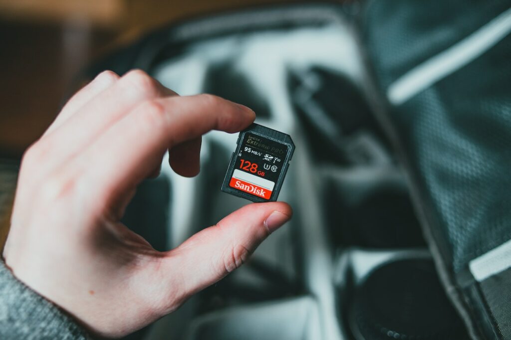 A person holds a black 128GB memory card and will put it in a black camera bag