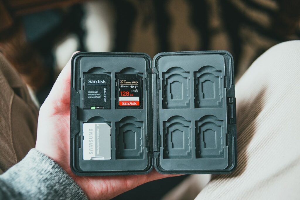 A person in sweatshirt and brown pants holding a black case containing a memory card and adapter
