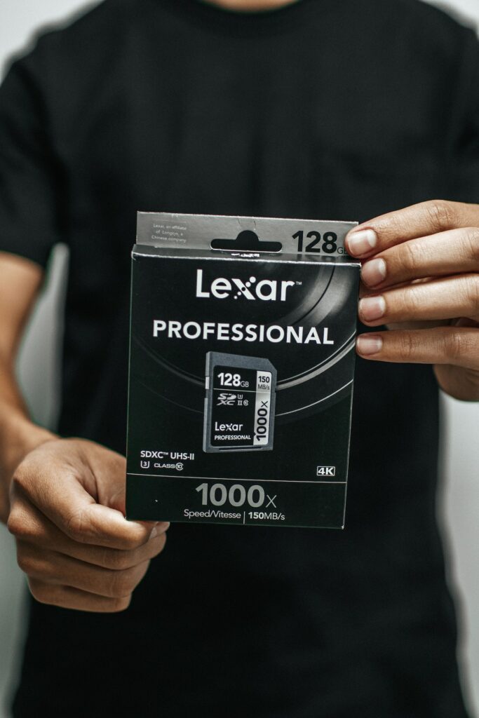 A person in a black t-shirt holds a box of a new Lexar 128GB memory card