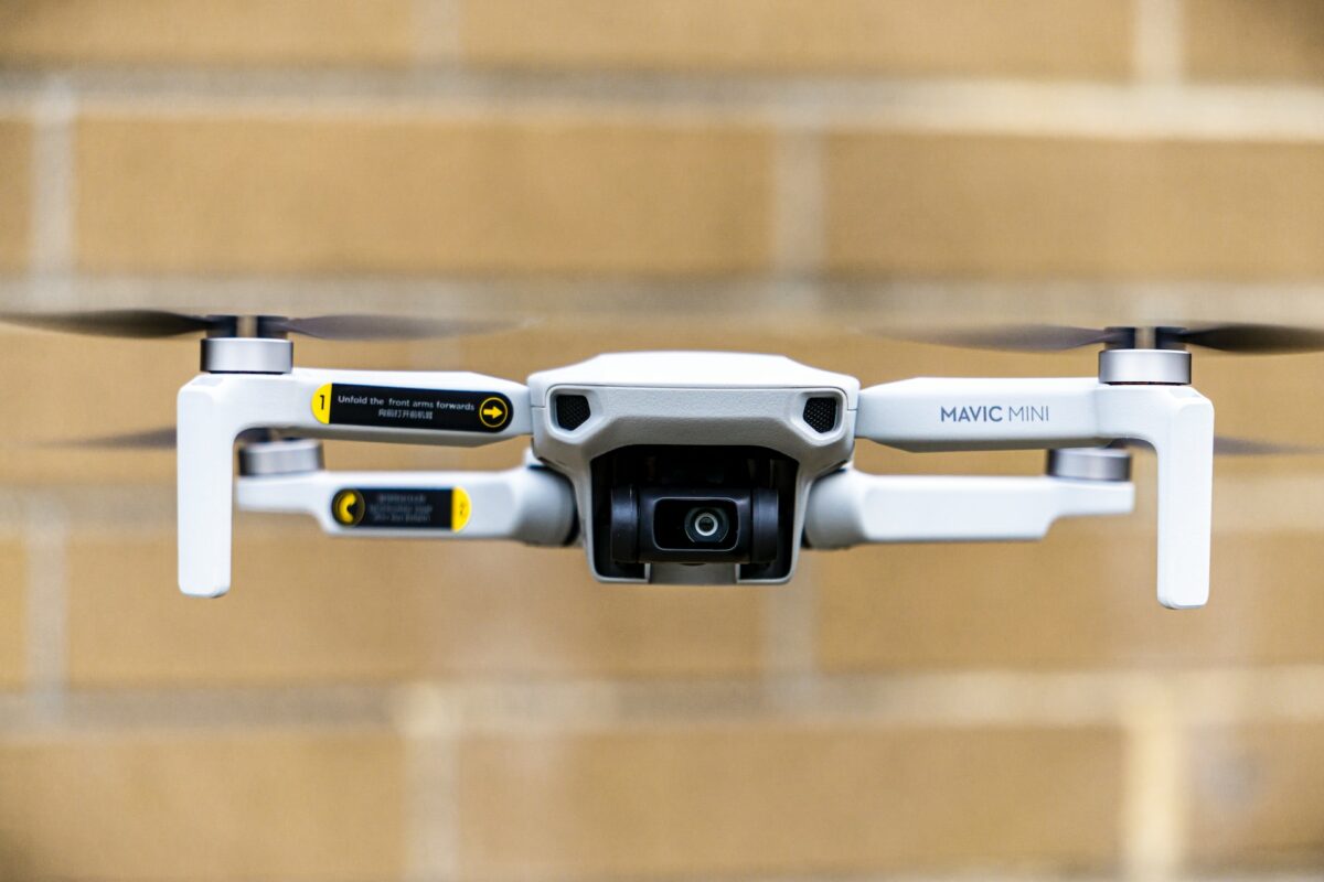 A black and white Mavic Mini with a black drone propeller near a yellow-bricked wall