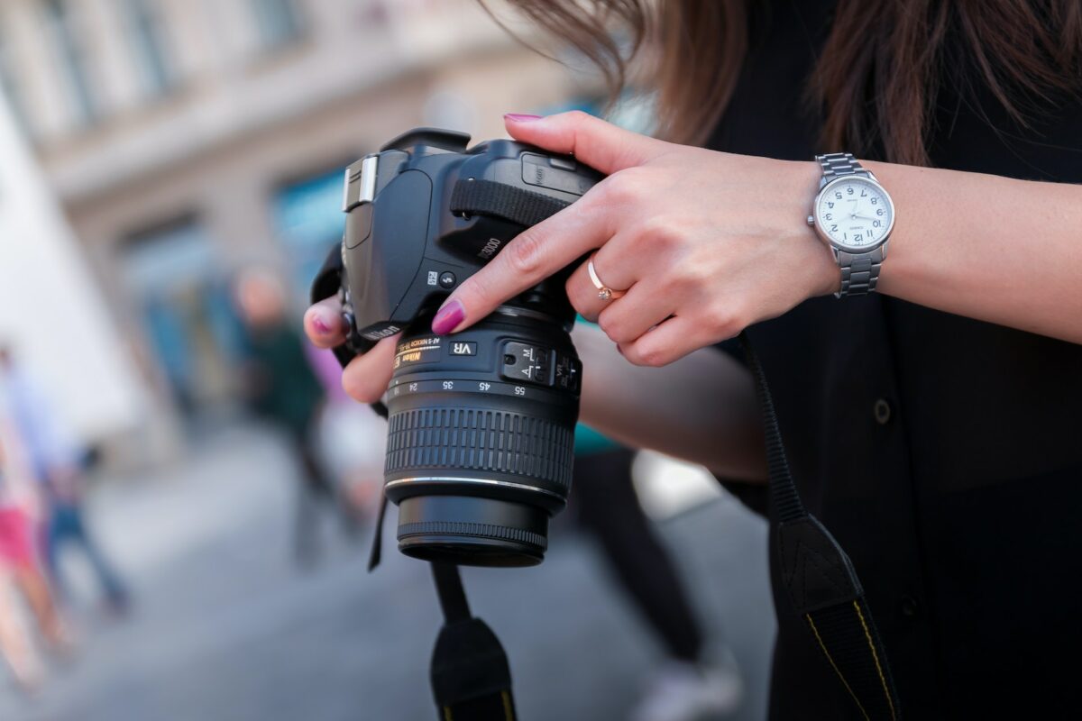 A woman wearing a gold ring and silver watch is holding a black DSLR camera