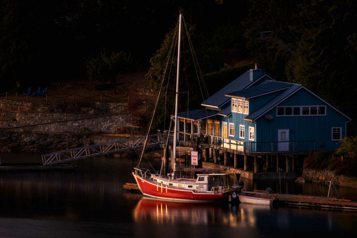 Red sailboat parked right near a blue house built on the edge of a lake