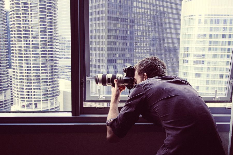 Man taking a photo outside, right inside the window of a building
