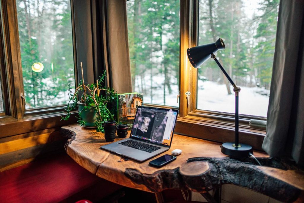 A wooden desk with laptop and phone near the window