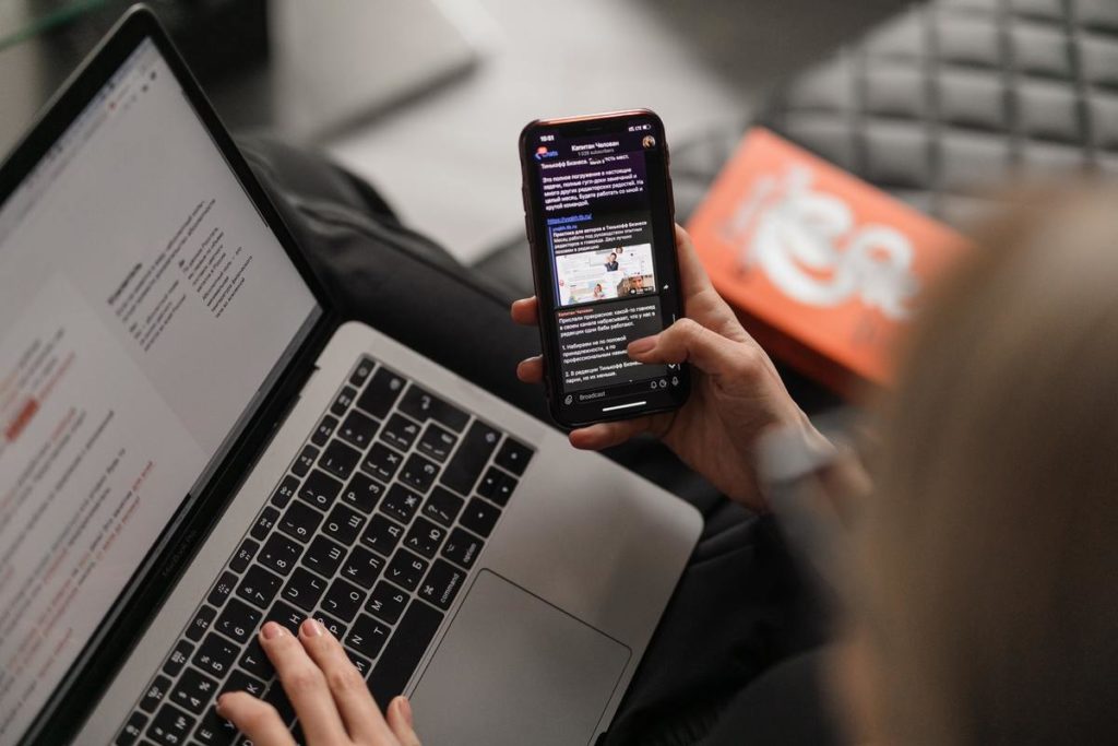 Person looking at phone while using laptop