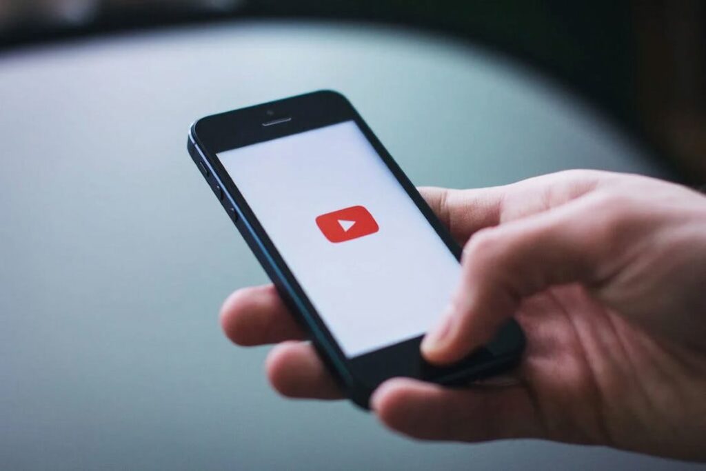 Person holding a black smartphone with its screen showing the red and white Youtube button