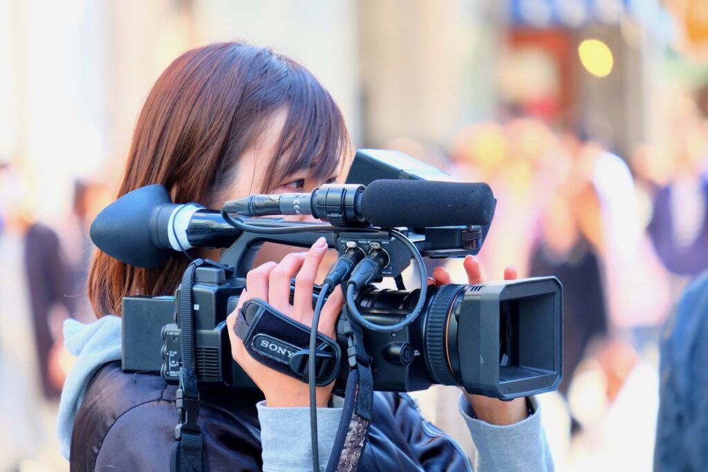 Woman wearing a silk purple and gray jacket while holding a large black video camera